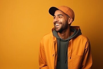 Portrait of a smiling man in a yellow jacket and cap on an orange background