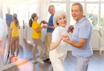 Happy smiling elderly woman enjoying impassioned merengue with male partner in latin dance class....