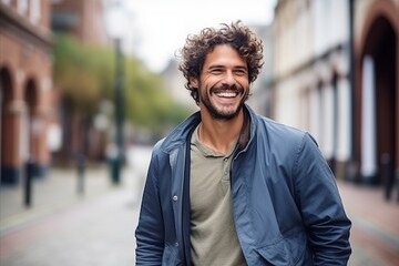 Portrait of a handsome young man with curly hair smiling at the camera - obrazy, fototapety, plakaty