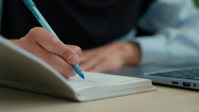 Close up female hand writing in notebook unrecognizable businesswoman muslim islamic woman in hijab student studying write notes tasks business paperwork financial budget with laptop on office desktop