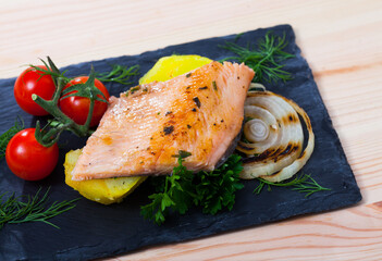 Roasted trout fillet served with baked potatoes, grilled onion, cherry tomatoes and greens..