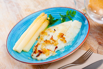 Deliciously roasted halibut fillet with asparagus and greens on blue plate