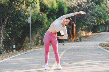 Athletic woman performs a side stretch on a serene park road, engaging in a healthy fitness routine.