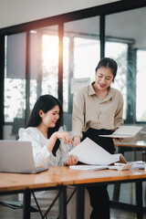 Two professional women engaging in a collaborative work discussion with laptops and notes on a bright office desk.