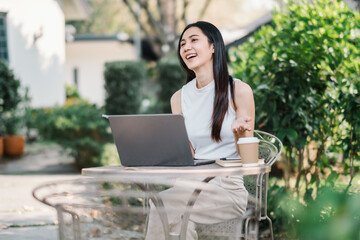 Cheerful woman enjoys working on her laptop at an outdoor table in a lush garden, embodying the freedom of freelancing.