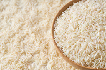Organic white basmati rice are scattered in a wooden bowl close up.
