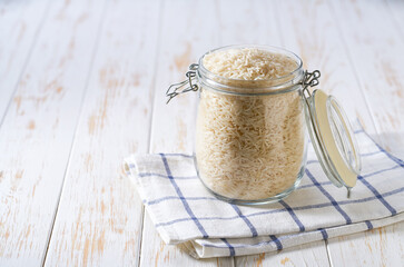 Raw long rice basmati in glass storage jar on a white wooden table.