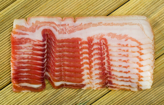 Closeup of thin slices of cured streaky side bacon on wooden surface..