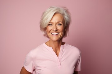 Mature woman with blond hair. Portrait of happy mature woman looking at camera and smiling while standing against pink background