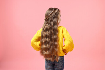 Little girl with braided hair on pink background, back view