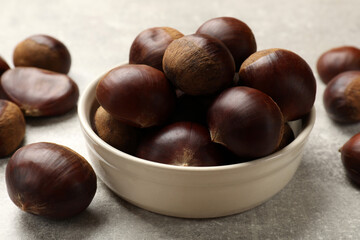 Bowl with roasted edible sweet chestnuts on light grey table, closeup