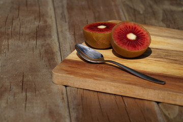 A delicious red kiwifruit sliced in half, with a teaspoon on a wooden surface