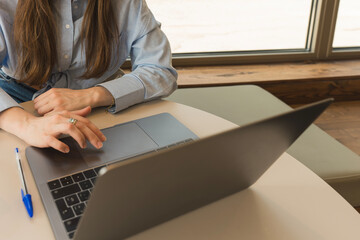 Unrecognizable woman in light blue shirt working in the office with her laptop