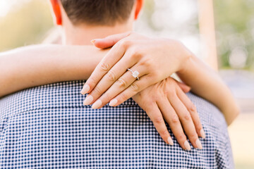 A couple in love are engaged and she's embracing him with her hands around his neck.