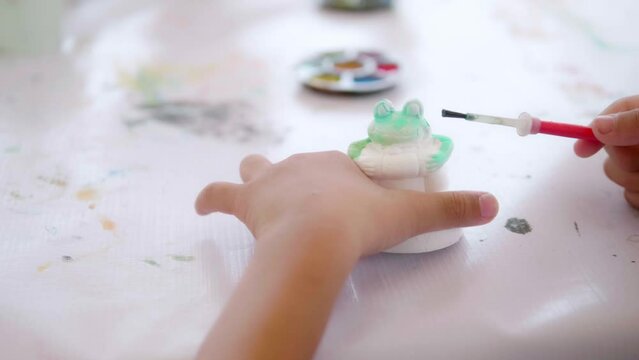 Cute Asian boy holding a paintbrush is painting watercolors on various shapes with preschool children, art class participants. Developing children's abilities, creative hobbies, day care activities