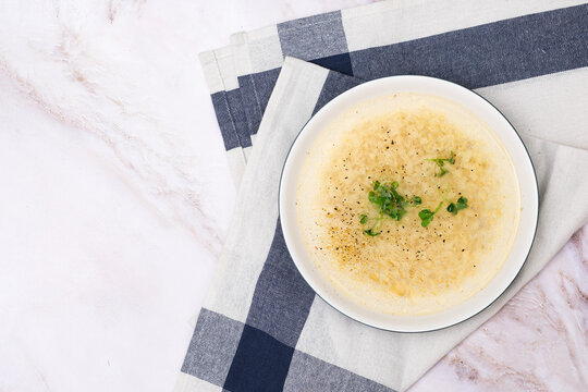 Instant chicken bone noodle soup in a white ceramic bowl isolated on white marble background. Parsley garnish.