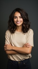 Fototapeta premium Portrait of young Mexican woman with pleasant smile and arms crossed isolated on gray wall with copy space Beautiful young woman with folded arms looking at camera against gray wall. isolated studio