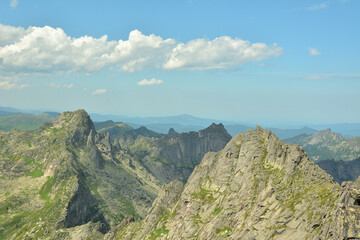 Pointed peaks of high sheer cliffs under a clear summer cloudy sky.