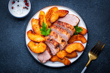 Baked pork tenderloin with spicy caramelized apples on plate, black table background, top view