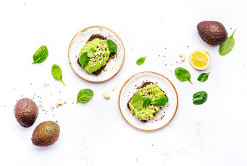 Avocado toasts with spinach and cashew nuts sprinkled with sesame seeds on white table background,...