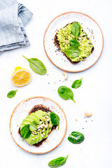 Avocado toasts with spinach and cashew nuts sprinkled with sesame seeds on white table background, top view