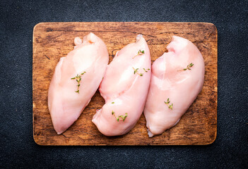 Raw chicken breast fillet on wooden cutting board, black table background, top view