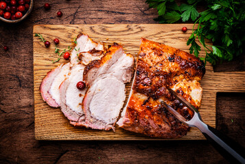 Baked festive pork butt or ham with herbs, spices and cranberries for sauce, served and sliced on cutting board, rustic wooden table background, top view
