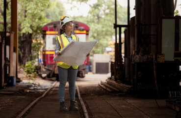 Portrait of railway technician worker in safety vest and helmet working with blueprint at train repair station