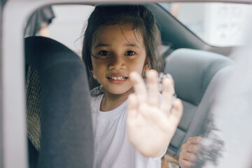 Little Asian girl waving goodbye while sitting in the passenger seat, ready to travel by the car.