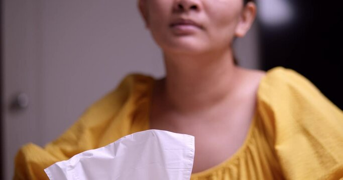 An Asian woman dressed in yellow cries then takes a tissue to wipe her tears. household problems. After having a fight with boyfriend. Woman Suffering From Depression Sitting In Living Room.