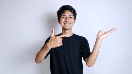 young asian man smiling gesturing right hand pointing left palm - obrazy, fototapety, plakaty