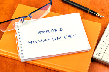 Latin quote Errare humanum est, meaning It is human nature to make mistakes. Mistakes are inherent in human existence. Text written on a clean white notebook