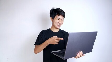 Excited young Asian man with gestures holding a laptop while pointing at the laptop