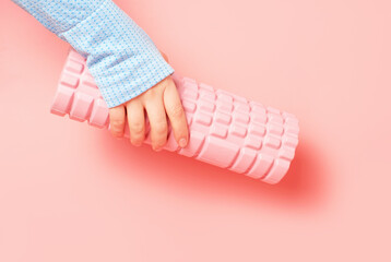 Female hand holding a massage roll on pink background close-up.
