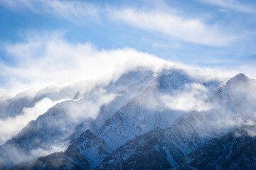 A closeup view of a mountain peak covered in snow as the wind swirls clouds around it. Aspen...