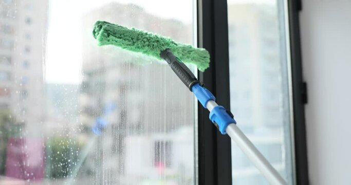 Cleaning windows with fluffy wet mop in high-rise office building