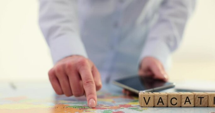 Woman index finger and cubes with word Vacation on world map