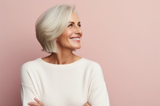Portrait of a beautiful middle-aged woman in a white sweater on a pink background