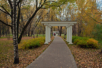 A path in an autumn park with a white gazebo in the background.