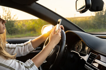 Woman sending messages with smartphone while driving automobile. Female driver using mobile phone...