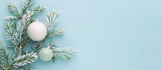 Fototapeta na wymiar Minimal Christmas concept with a snowy fir branch and white ornament. Flat lay horizontal composition on a pastel blue background, featuring a top view with empty space for writing.