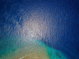 Top down aerial view of blue water and a tropical coral reef in a warm ocean