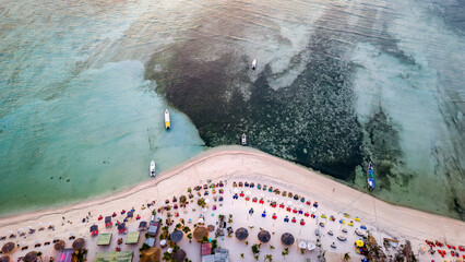 Top down aerial view of tables and seats on a tropical sandy beach during sunset on a small island