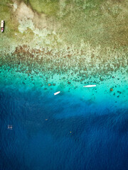 Aerial view of traditional outrigger type boats with snorkelers and swimmers over a tropical coral reef in a clear, warm ocean
