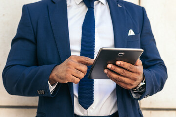Unrecognizable black businessman in a suit using a tablet outside.