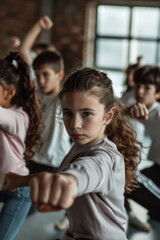 A young girl with a serious expression, wearing a white shirt, stands confidently with a group of children, demonstrating self-defense moves, symbolizing empowerment