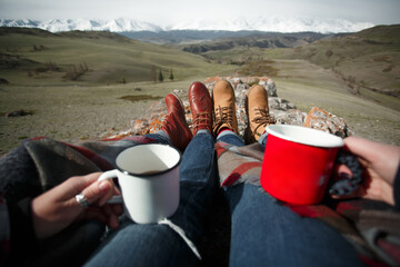 Close-up of hands with mugs and feet against background of mountains. First-person view - 766808040