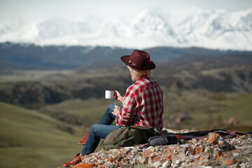 Girl traveler with hat and mug on background of mountains - 766808280