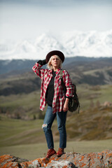 Hipster girl traveler with hat and backpack on background of mountains - 766808628