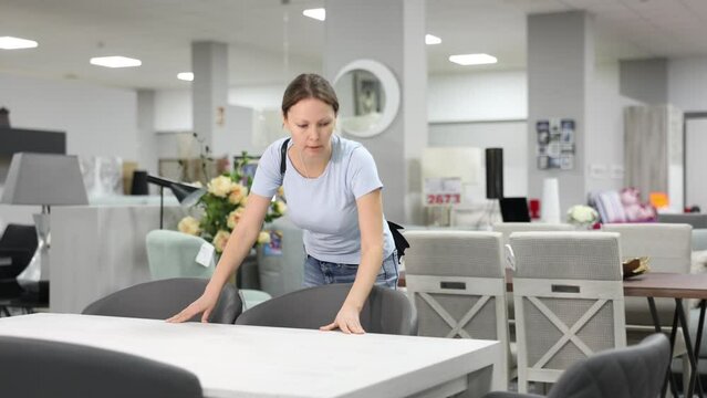 Female customer choose dining table desk in furniture store showroom. Woman runs hand over smooth surface, imagining how it would look in dining room 